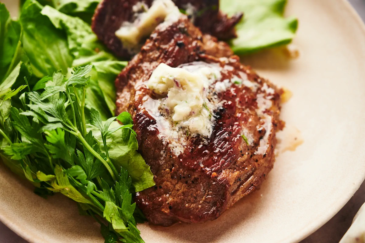 A focused shot of flat iron steak with herb butter and fresh greens.