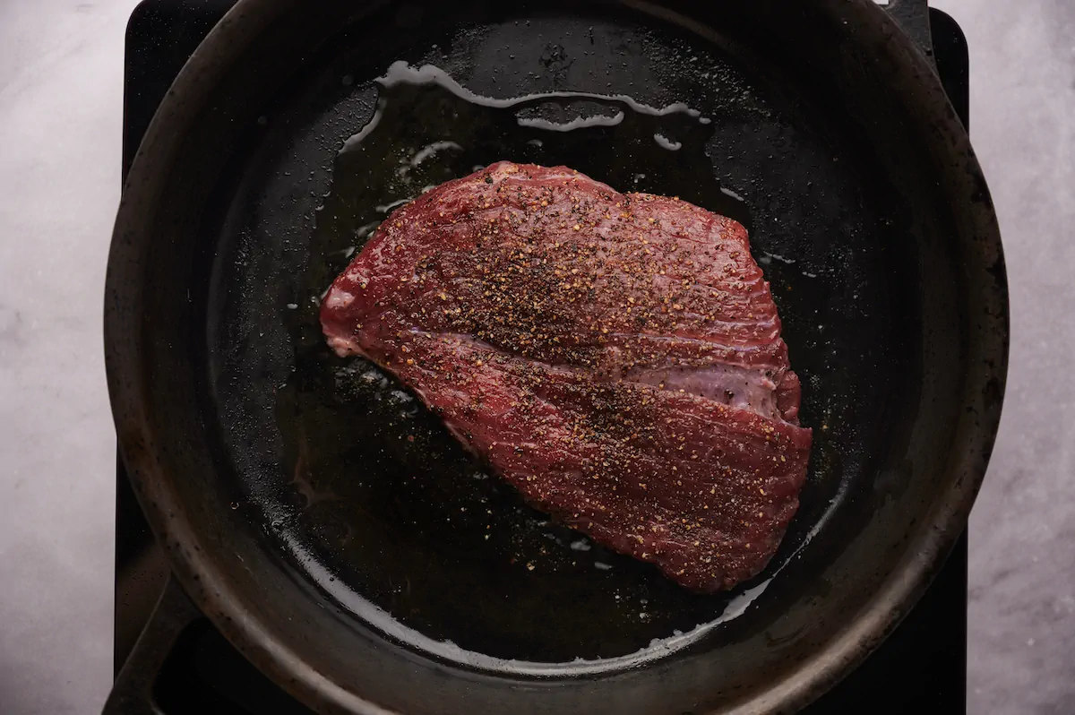 Seasoned flat iron steak cooking in a cast iron skillet.