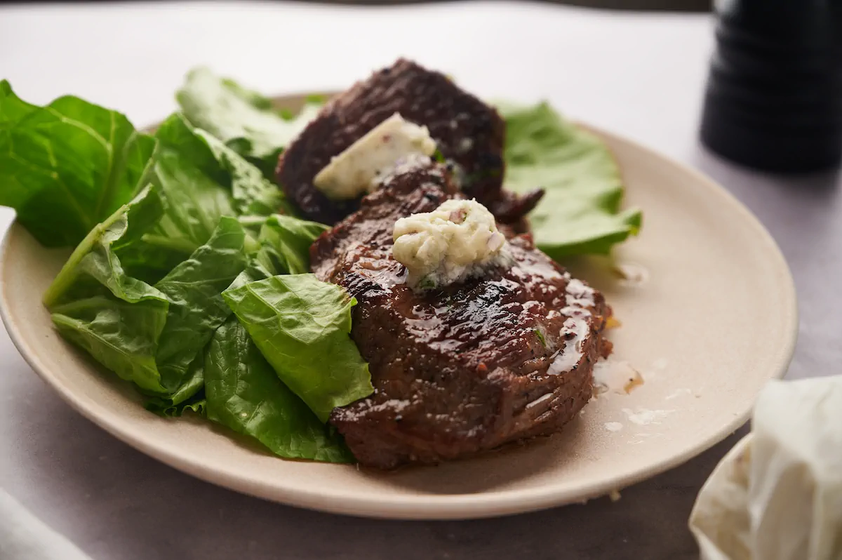 A plate featuring a perfectly cooked flat iron steak with herb butter and greens.