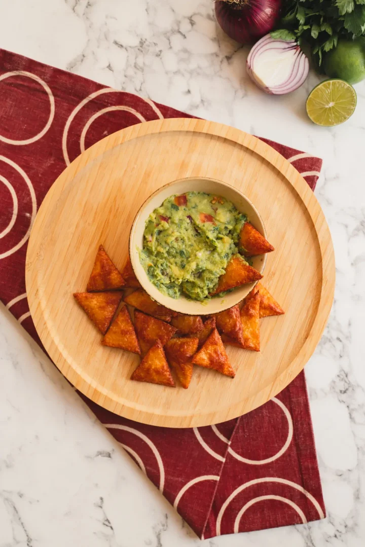 Guacamole dip in a bowl with keto tortilla chips on a wooden plate.