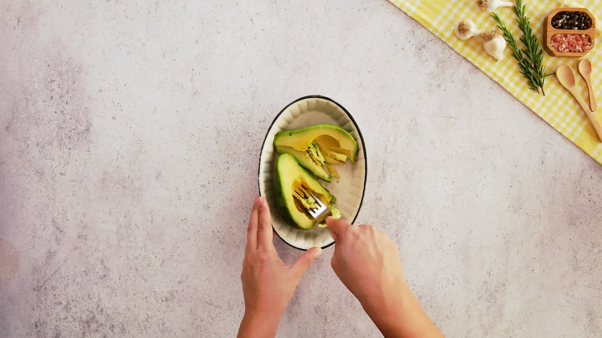 Mashing ripe avocado with a fork in a bowl.