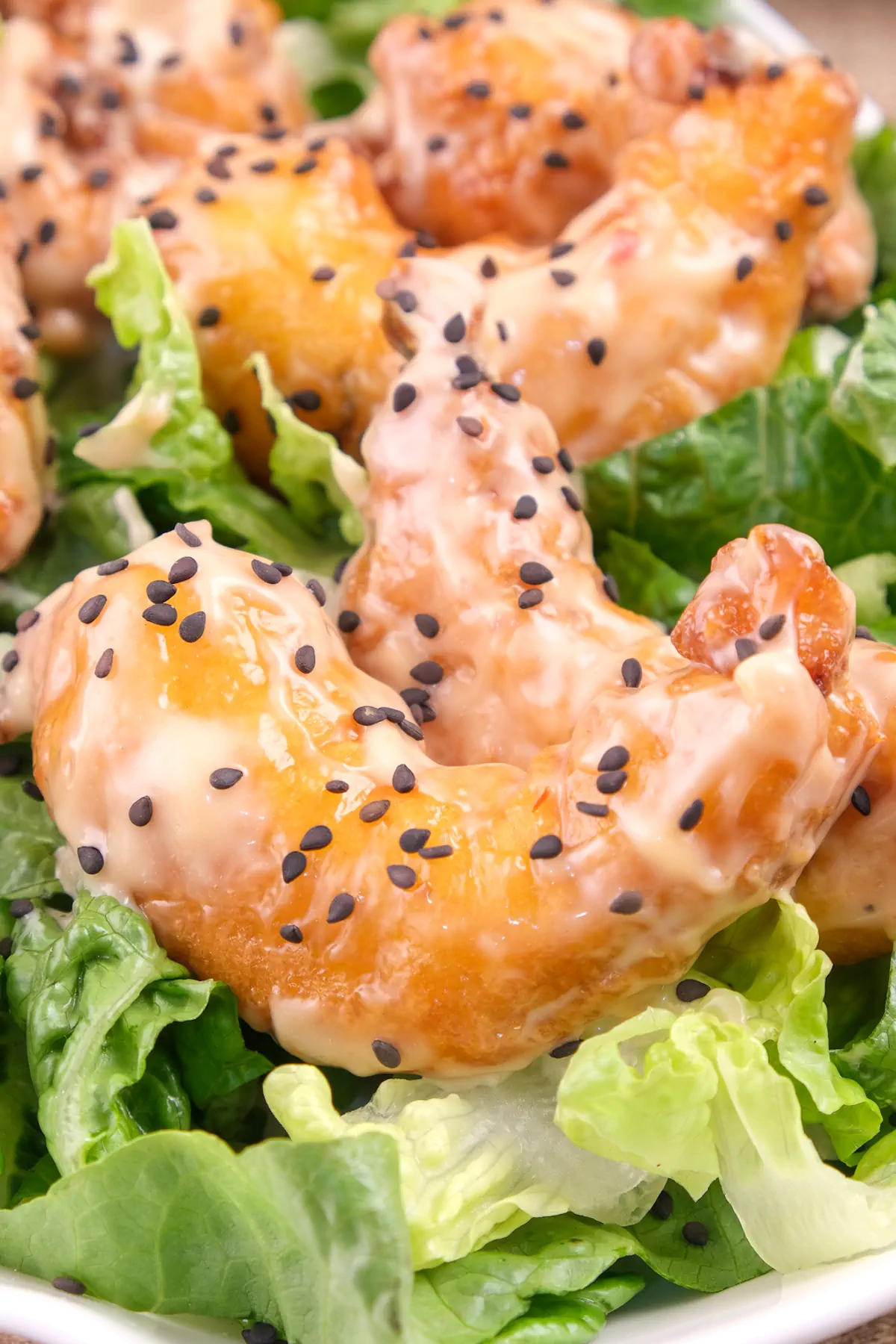 Keto bang bang shrimp garnished with toasted black sesame seeds and served on fresh lettuce leaves.