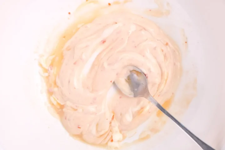 Mixing Japanese mayonnaise with other sauces with a spoon to make the bang bang sauce.