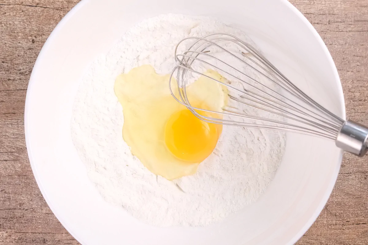 Egg has been added to the dry ingredients mix for the batter in a big bowl with a whisk.