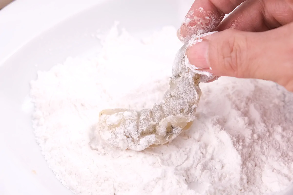 Lightly coating a shrimp in coconut flour with a hand.