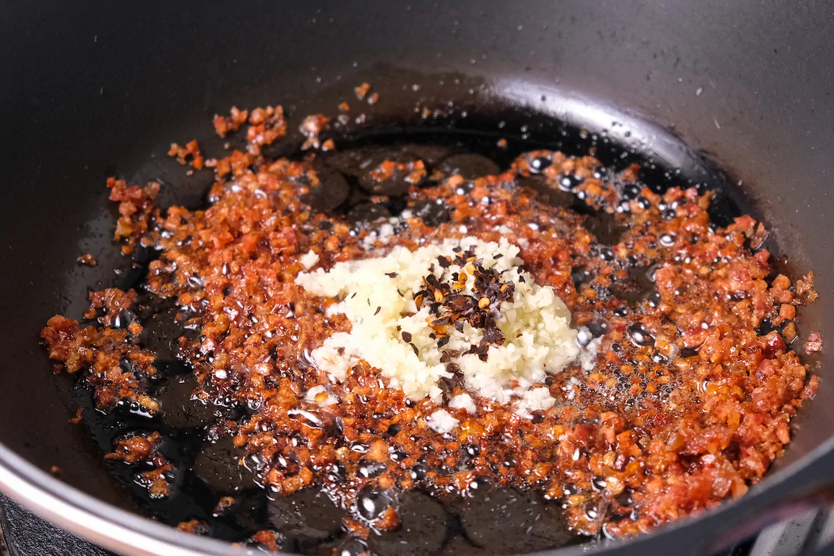 Adding garlic and red pepper flakes to the chorizo cooking in hot pan.