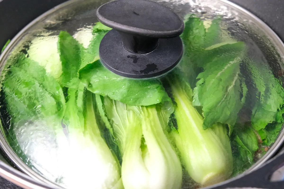 Cooking chorizo and bok choy in a pan and covered with a lid.