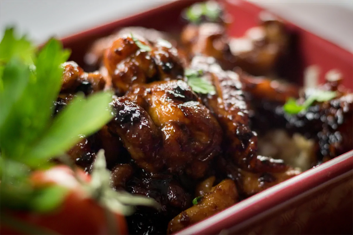 A close-up shot of chicken glazed with bourbon sauce in a red serving dish and garnished with green herbs.