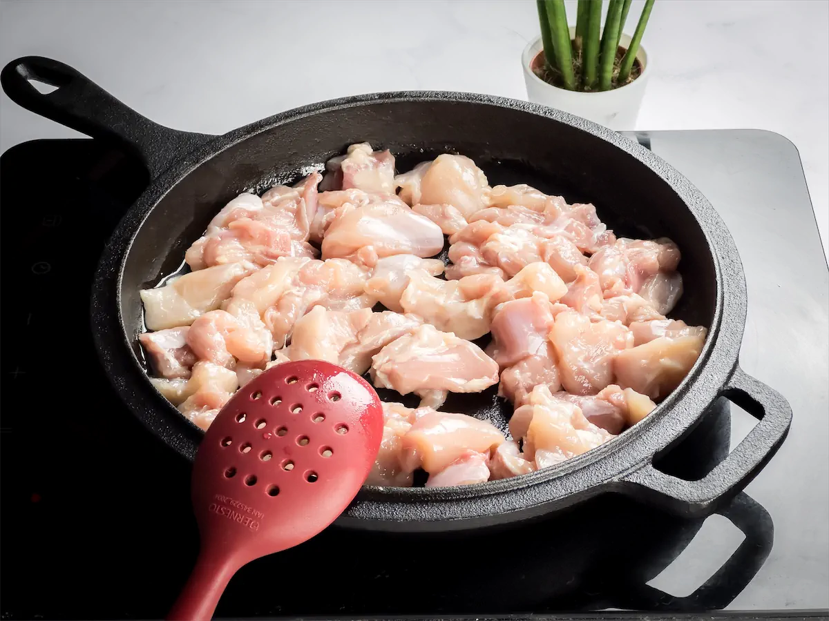 Skinless, boneless chicken pieces are getting cooked in a cast iron skillet with avocado oil.