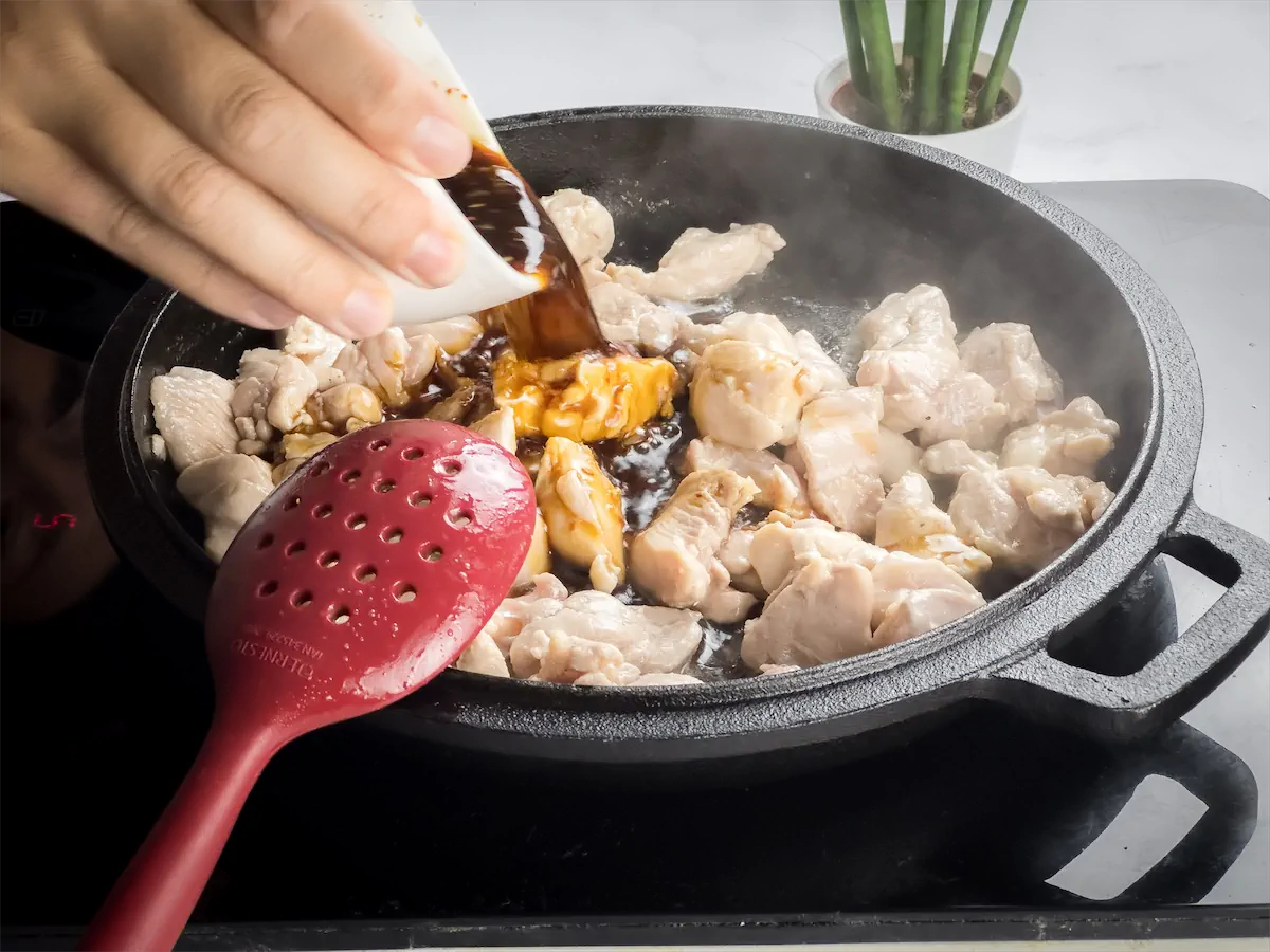 A hand pouring the prepared sauce mix into the chicken cooking in the cast iron skillet.