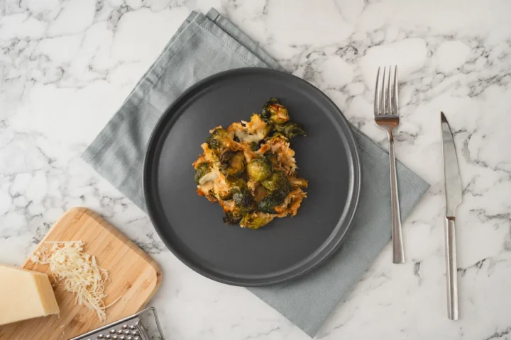Cheesy keto Brussels sprouts served on a plate with a fork and a knife.