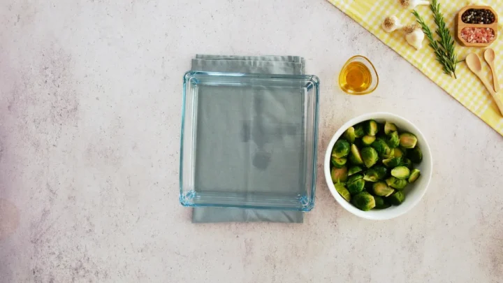 An empty baking dish alongside a bowl of halved Brussels sprouts and olive oil.