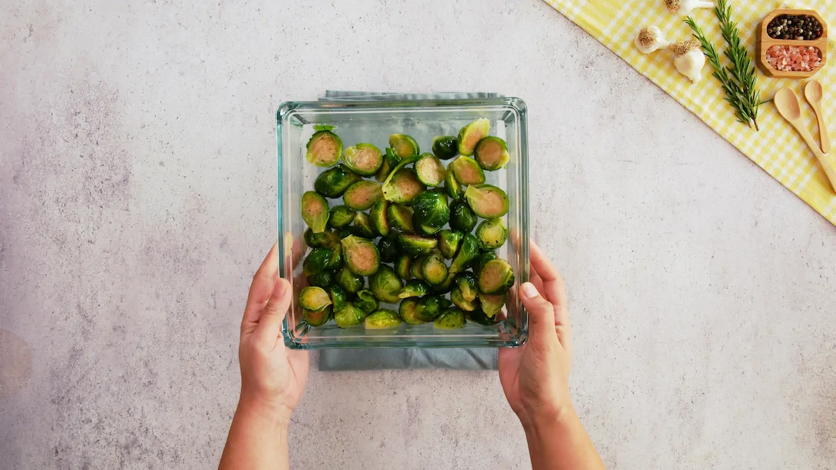 Halved Brussels sprouts tossed with olive oil and seasoning in a baking dish.