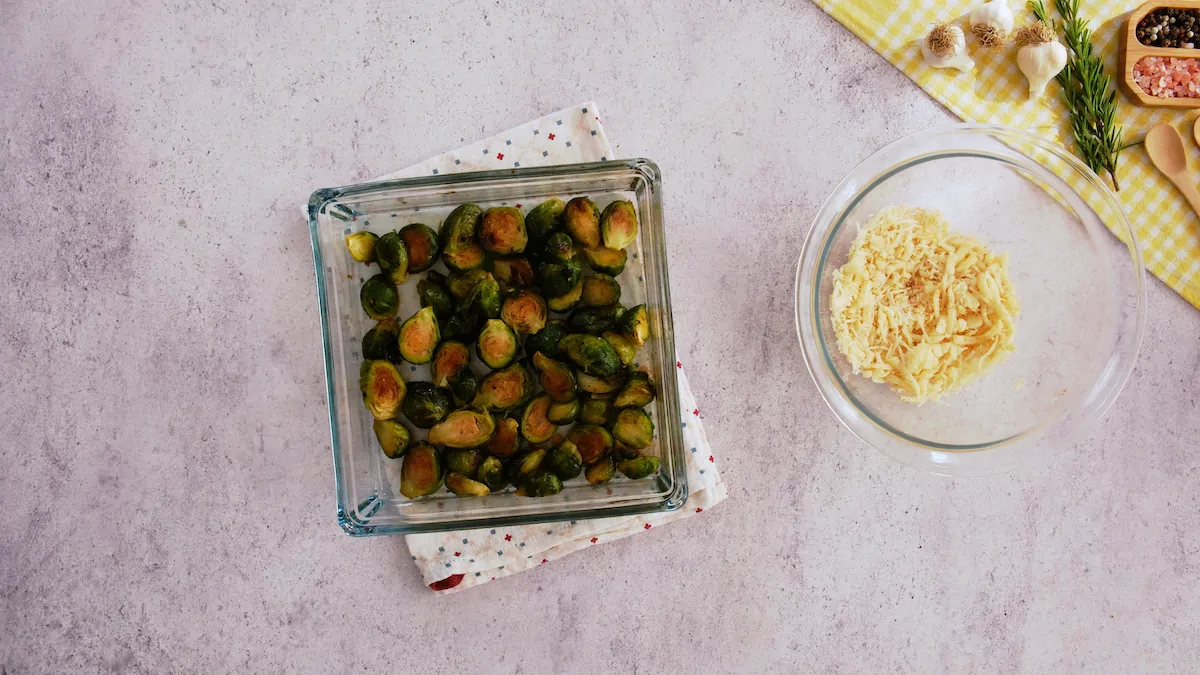 Roasted Brussels sprouts in a baking dish beside a bowl of cheese and spice mixture.