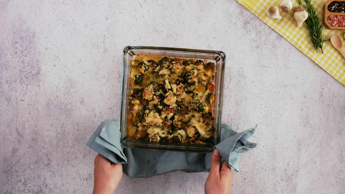 Two hands holding a hot Brussels sprouts casserole in a baking dish just out of the oven.
