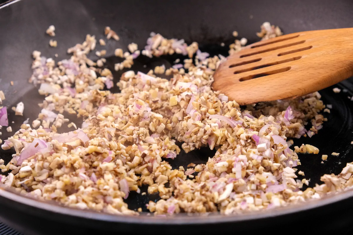 Cooking the finely chopped mushrooms and shallots in a pan for the filling.