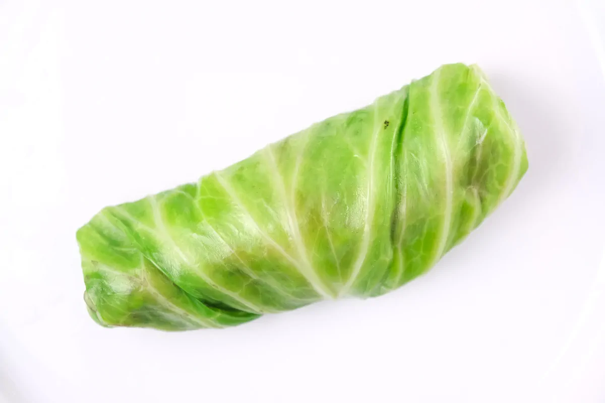 A perfectly wrapped cabbage roll on a plate, ready to be cooked.