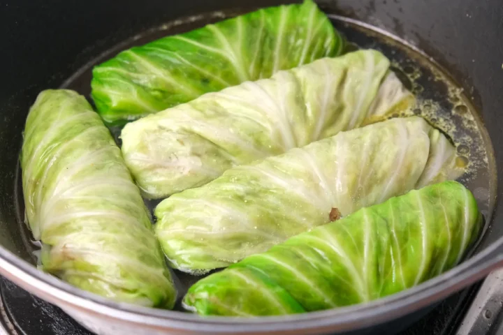 Cabbage rolls cooking in a pan with chicken stock.