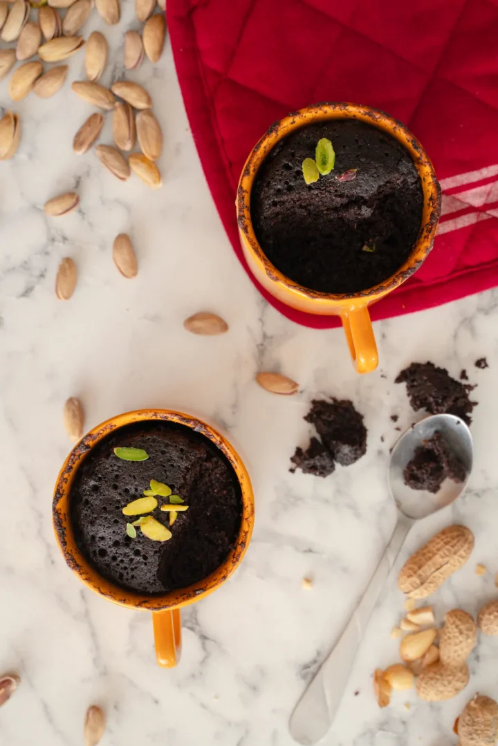 Homemade keto chocolate mug cakes, garnished with nuts and a spoonful taken out from each mugs.