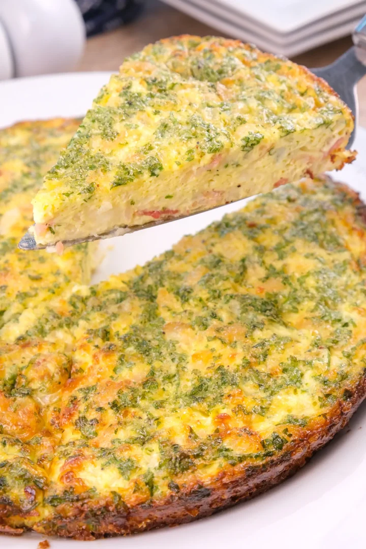 A pie cut from a round homemade crustless quiche and lifted, revealing the texture inside.