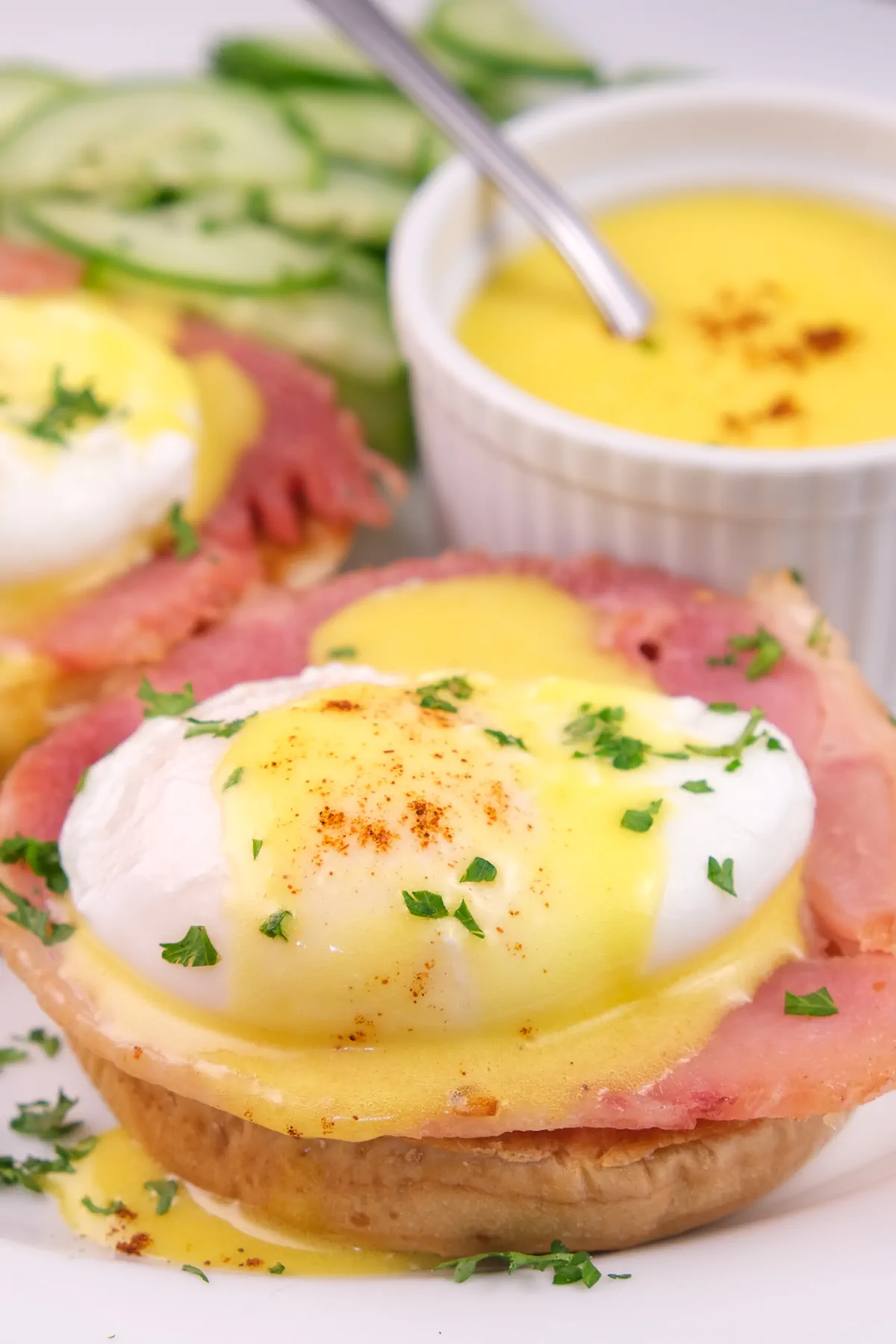 Eggs Benedict on a plate, accompanied by a bowl of keto hollandaise sauce.
