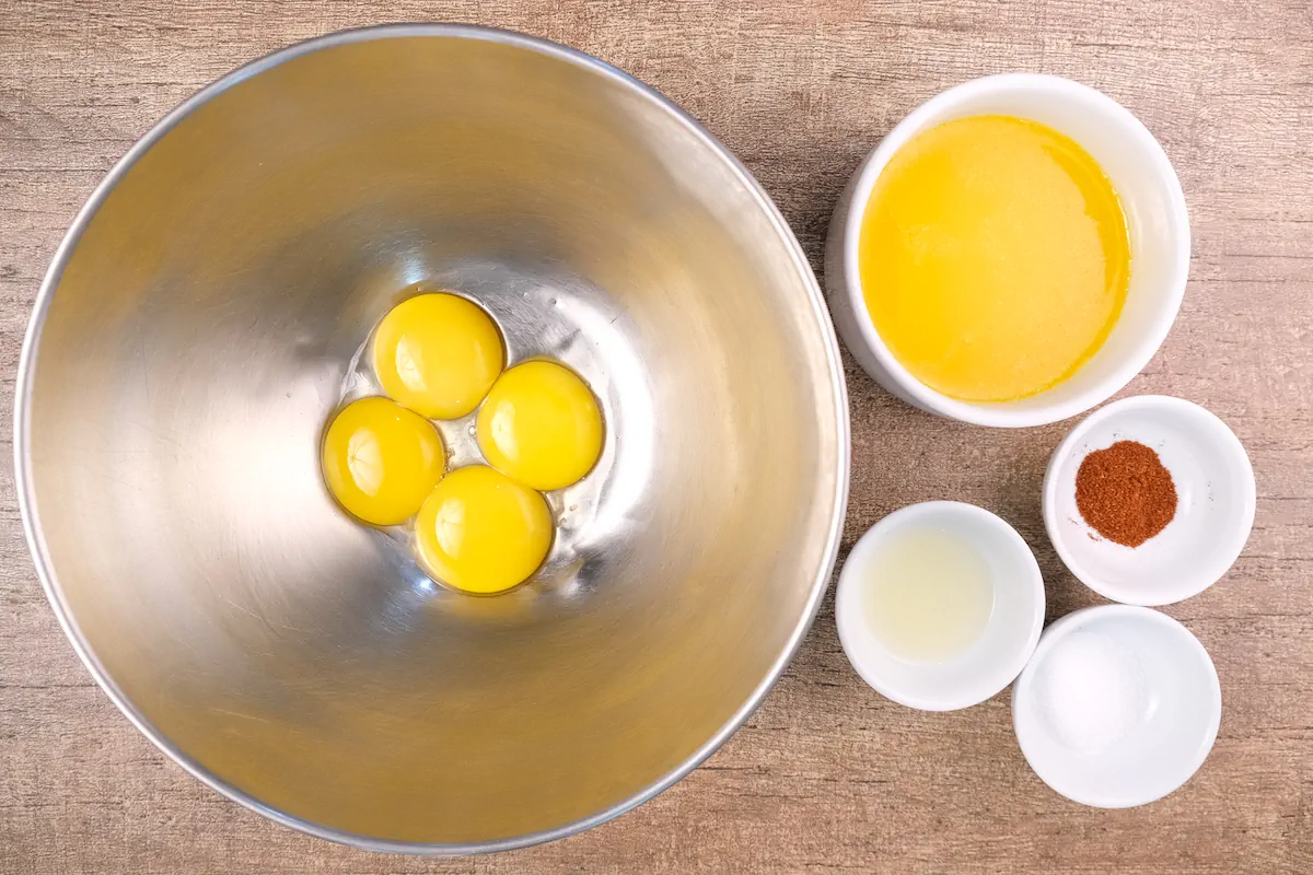 All the ingredients required to keto hollandaise sauce including egg yolks, fresh lemon juice, melted butter, sea salt, and cayenne pepper gathered and arranged on the table.
