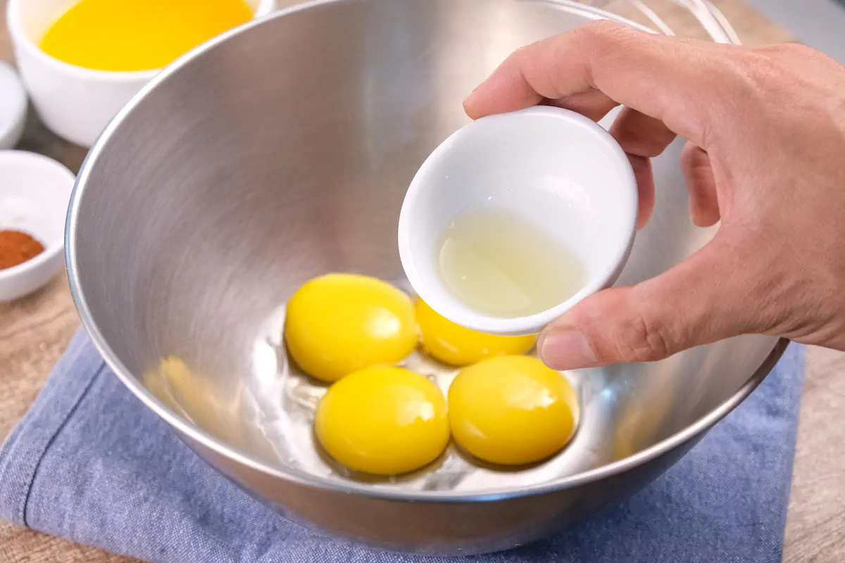 Adding fresh lemon juice to the mixing bowl with egg yolks.