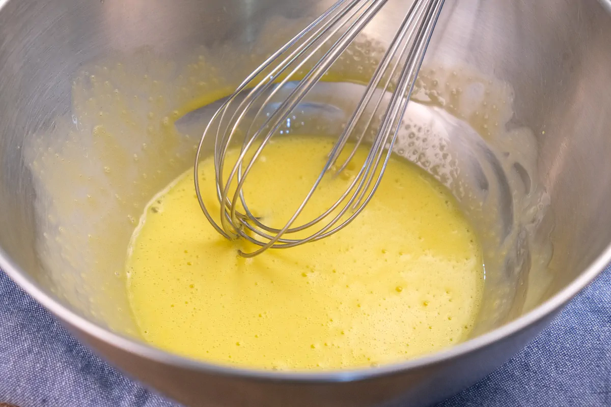 Whisking egg yolks with lemon juice in a stainless steel mixing bowl.