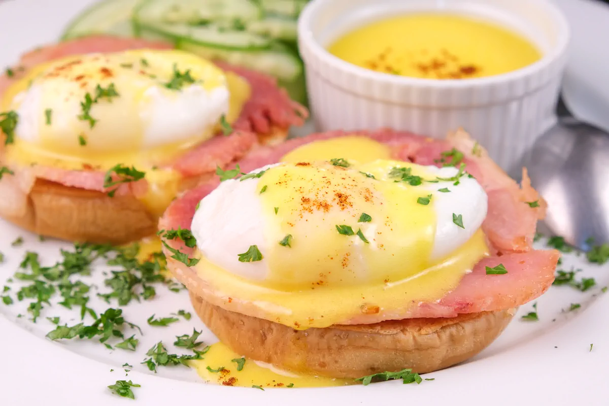 Eggs Benedict with homemade keto hollandaise sauce served on a plate alongside a bowl of the same sauce.
