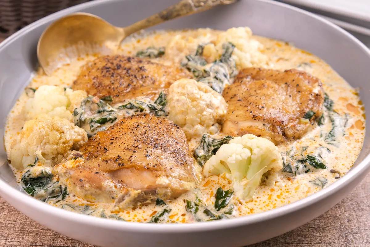 Homemade keto pesto chicken with veggies presented in a bowl and a spoon.