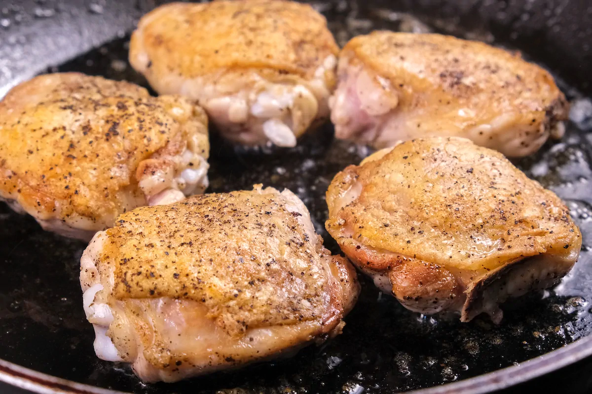 Chicken thighs cooking in a cast-iron skillet.