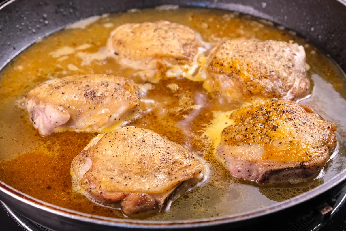Chicken thighs are getting cooked with chicken stocks in a cast-iron skillet.