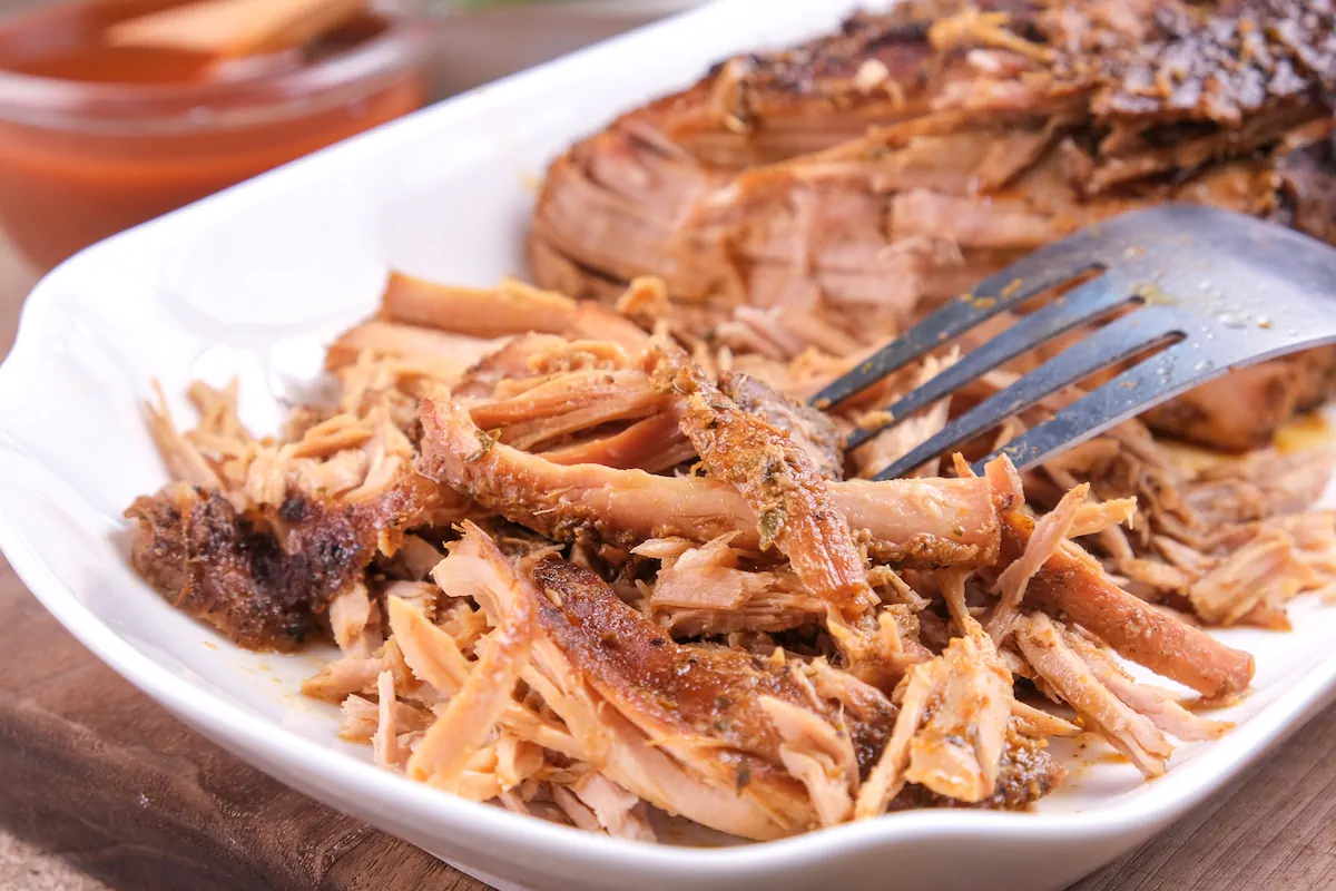 Low-carb keto pork cooked in slow cooker getting shredded with a fork.
