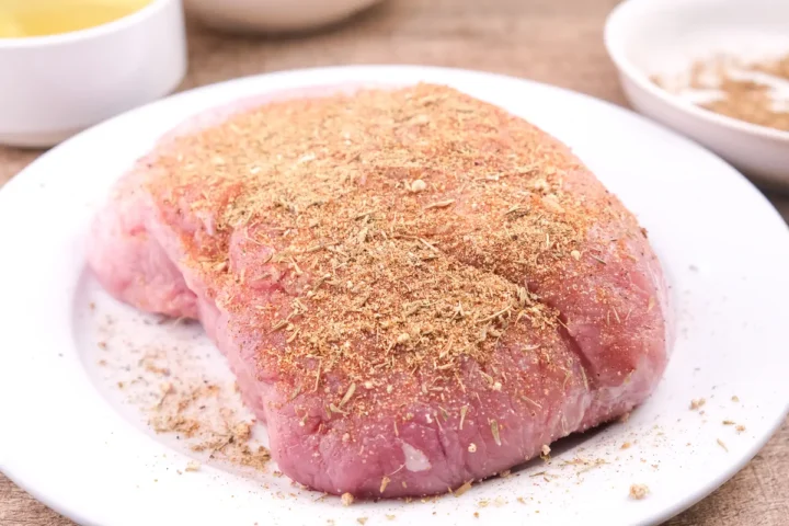 Sprinkling the spice mixture onto the pork butt roast.