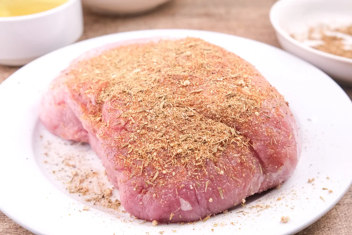 Sprinkling the spice mixture onto the pork butt roast.