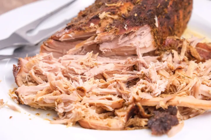 Shredding keto pulled pork with a fork on a plate.