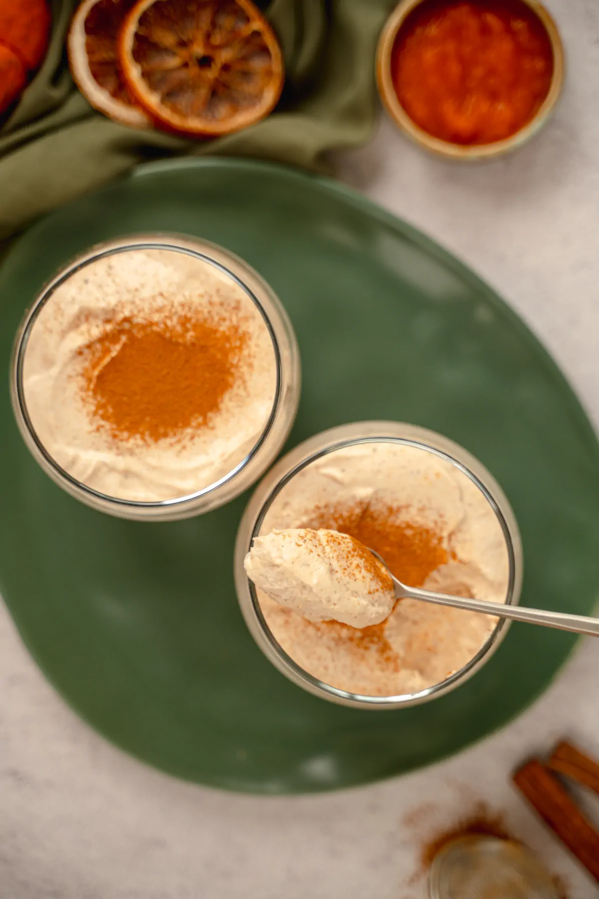 Homemade keto pumpkin cheesecake mousse served in two transparent glasses garnished with cinnamon powder, where one glass remains untouched, while some portions is eaten from the other glass and a spoonful is ready to be eaten too.