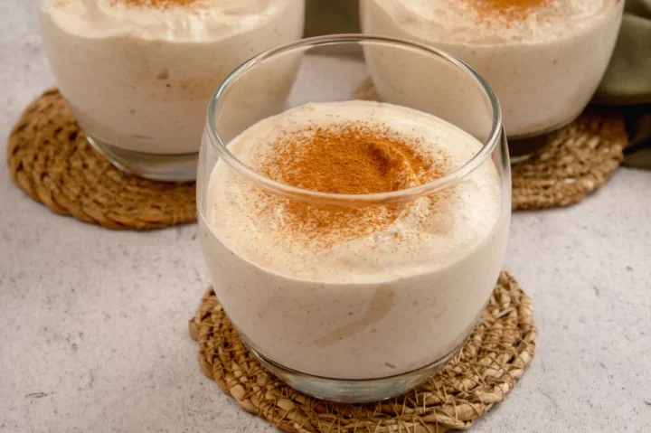A focused picture of keto pumpkin cheesecake mousse in a clear glass dusted with cinnamon while two glass of the same is in the background.