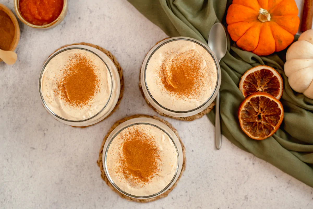 Three transparent glasses filled with keto pumpkin cheesecake mousse, topped with a dash of cinnamon.