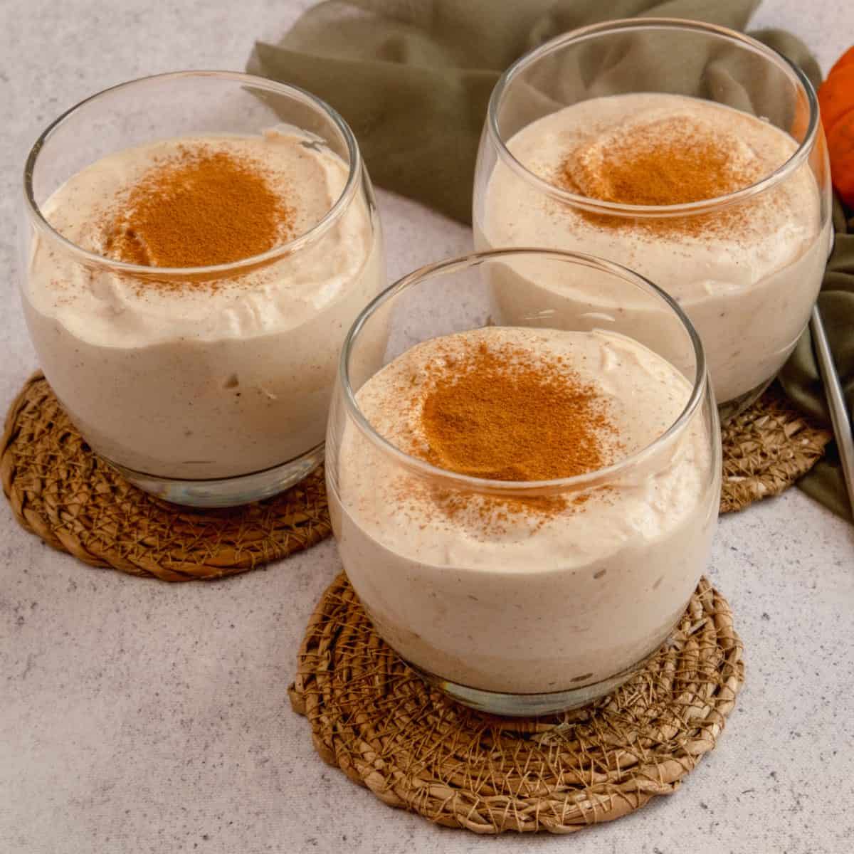 Three clear glasses with keto pumpkin cheesecake mouse garnished with cinnamon powder.