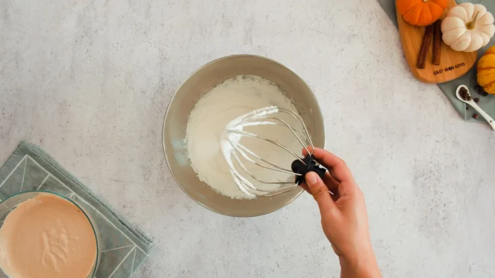 Removing the whisk attachment from the stand mixing bowl with heavy cream and powdered erythritol mixture.