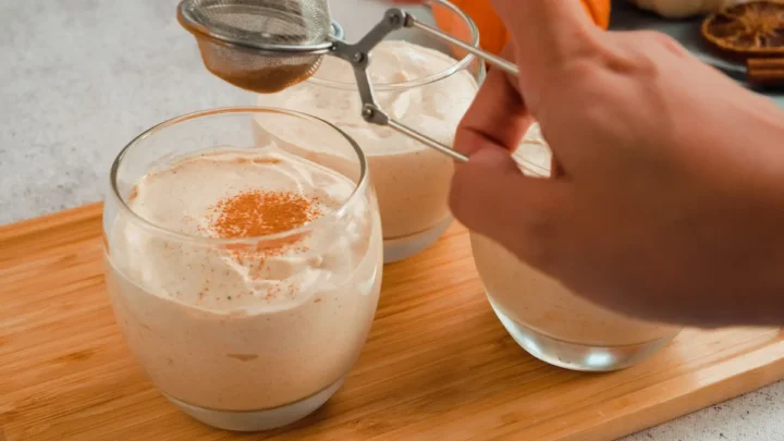 Dusting the cinnamon powder on top of the pumpkin cheesecake mouse in clear glasses.
