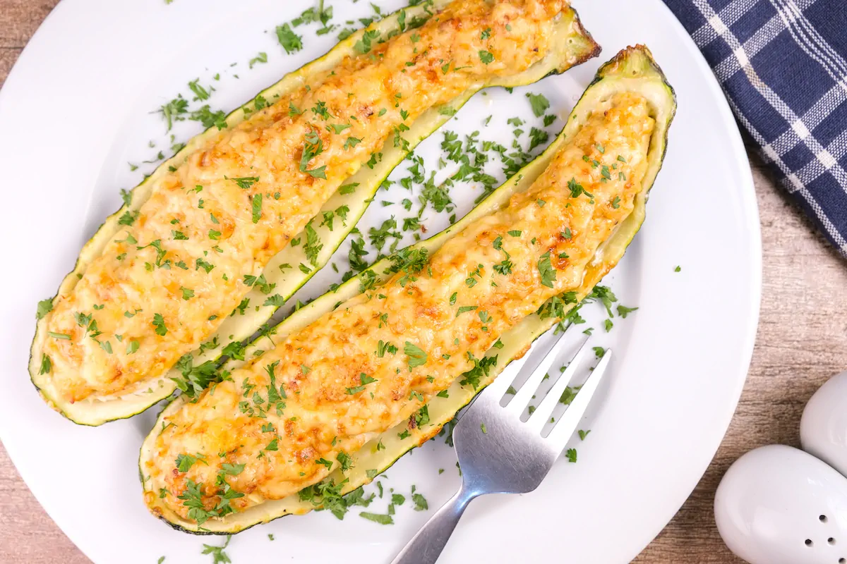 Keto stuffed zucchini boats with chicken and pesto served on a plate with a fork.