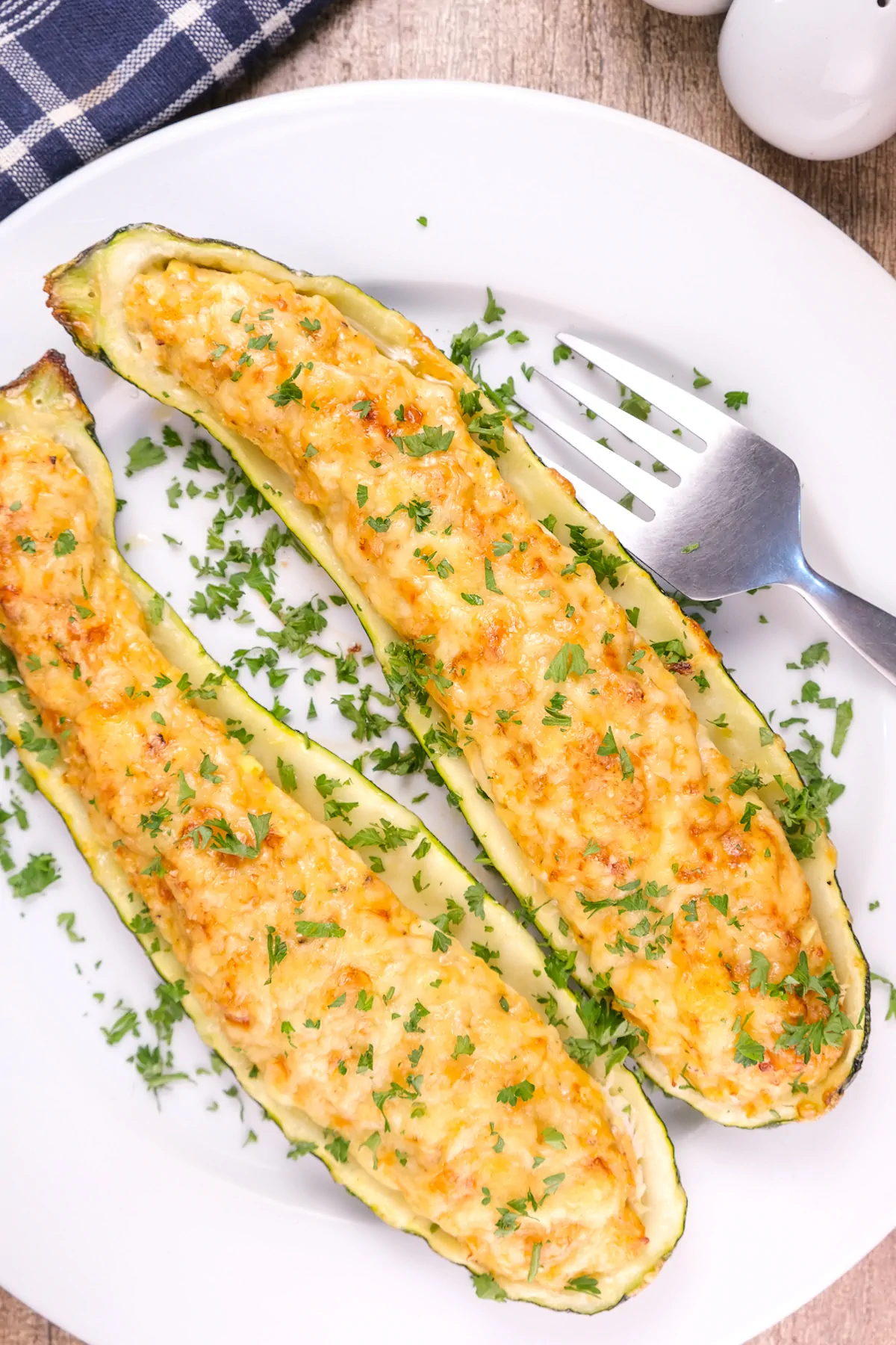 Keto stuffed zucchini boats served on a plate and garnished with chopped fresh herbs.