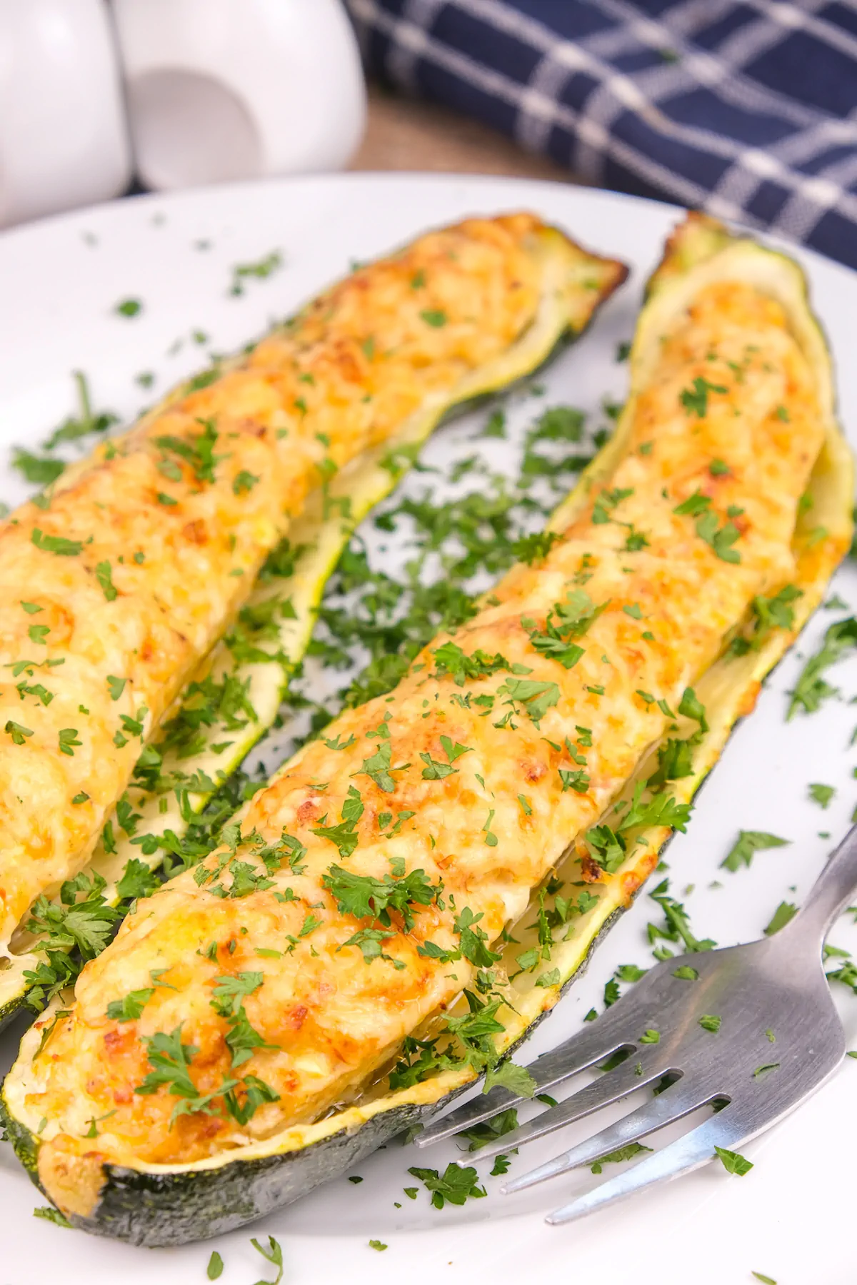 Keto zucchini boats filled with chicken and pesto and garnished with fresh herbs on a plate.
