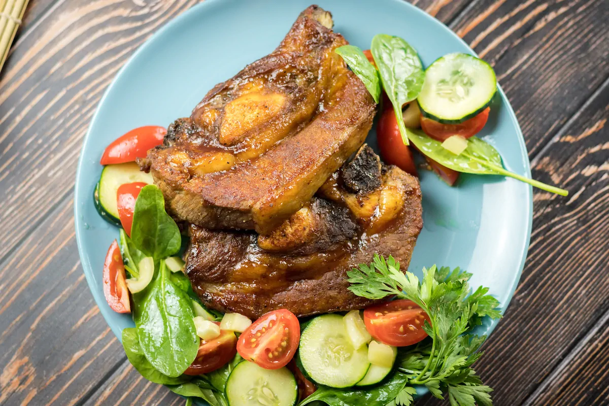 Oven-baked beef ribs accompanied with fresh salad served on a plate.
