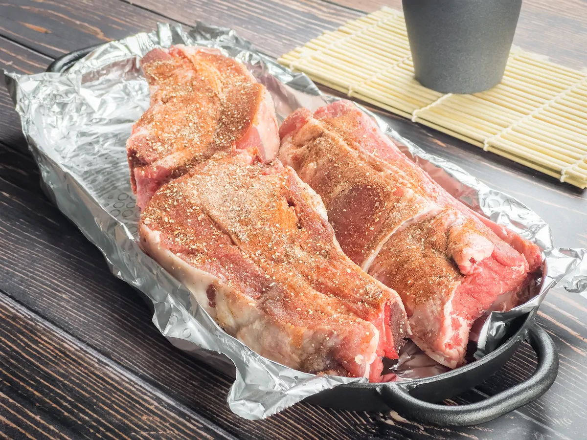 Beef ribs rubbed with dry spices on a baking tray lined with aluminum foil