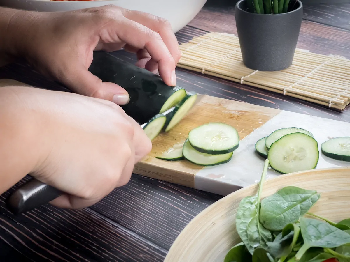 Slicing cucumbers on a chopping board with a knife.