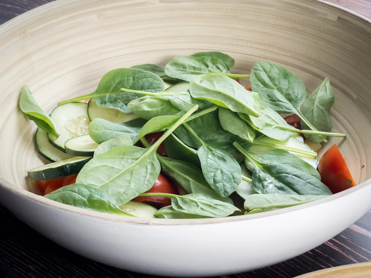 Adding fresh baby spinach to the bowl with cucumbers and tomatoes for the salad.