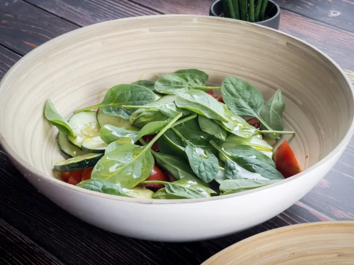 Olive oil drizzled onto the bowl with baby spinach, cucumbers and tomatoes.